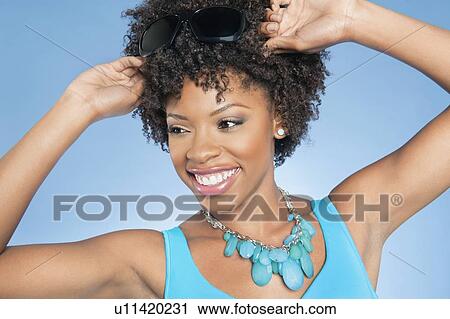 Happy African American woman adjusting sunglasses while looking away over colored background View Large Photo Image Stock Image - Happy African American woman adjusting sunglasses while looking away over colored background. Fotosearch