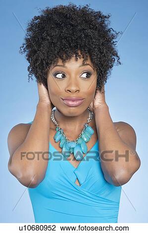 Stock Image - Happy African American woman covering ears over while looking away colored background. Fotosearch