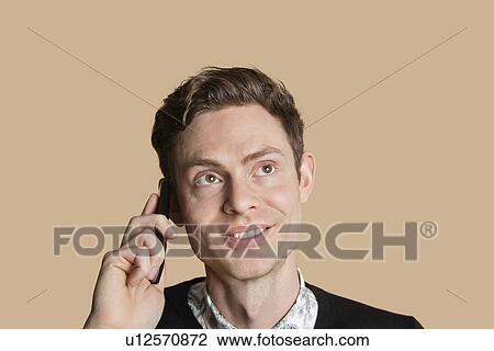 Stock Image - Happy mid adult man listening to mobile phone over colored background. Fotosearch