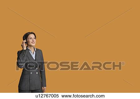 Stock Photography - Happy mid adult woman standing while listening to music on headphones. Fotosearch