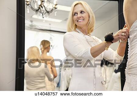 Stock Photo - Happy senior owner with pincushion in wrist helping bride getting dressed. Fotosearch