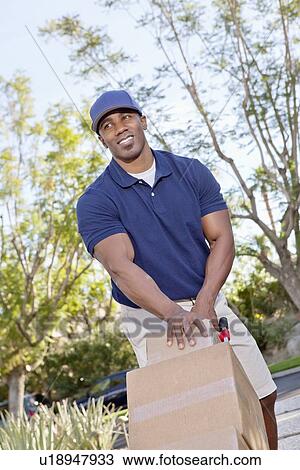 Stock Image - Happy young African American male pushing handtruck. Fotosearch