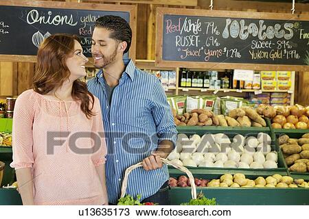 Stock Image - Happy young couple shopping together for vegetables in market. Fotosearch