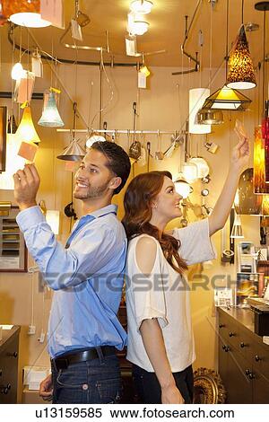 Happy young couple standing back to back while looking at price tag in lights store View Large Photo Image Stock Photography - Happy young couple standing back to back while looking at price tag in lights store. Fotosearch