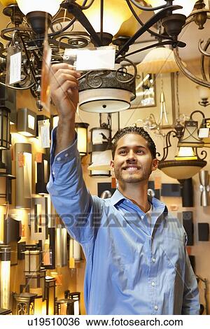 Happy young man looking at price tag of chandelier in lights store View Large Photo Image Stock Photograph - Happy young man looking at price tag of chandelier in lights store. Fotosearch