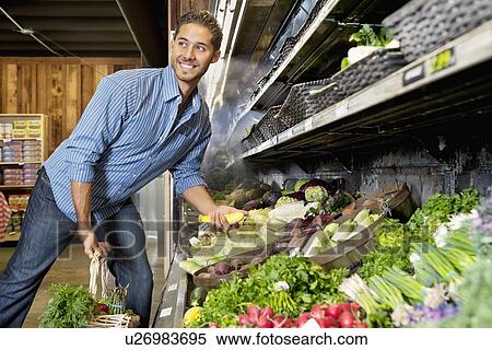 Stock Photography - Happy young man shopping for vegetables in market. Fotosearch