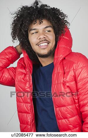 Happy young man wearing hooded jacket while looking away over colored background View Large Photo Image Stock Photo - Happy young man wearing hooded jacket while looking away over colored background. Fotosearch