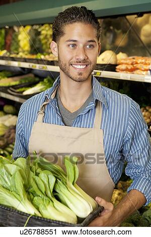 Stock Image - Happy young sales clerk holding bok choy in supermarket. Fotosearch
