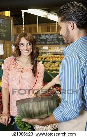 Stock Image - Happy young woman looking at store clerk in supermarket. Fotosearch