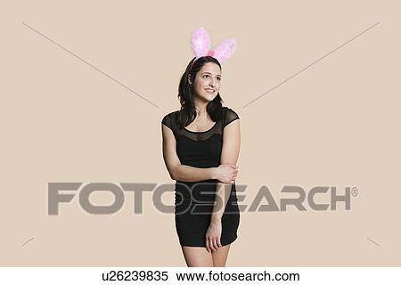 Stock Photography - Happy young woman wearing rabbit ears looking away over colored background. Fotosearch