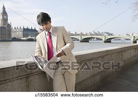 Picture - Indian businessman reading newspaper with buildings in background. Fotosearch