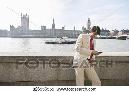 Stock Photography - Indian businessman text messaging with watercraft and buildings in background. Fotosearch