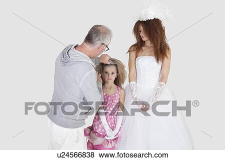 Stock Photo - Makeup artist with spraying on bridesmaid's hair while bride looking over gray background. Fotosearch