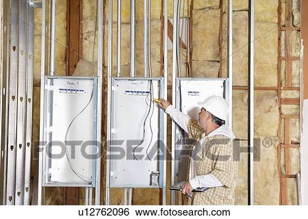 Stock Photograph - Male construction worker checking electric meters at construction site. Fotosearch