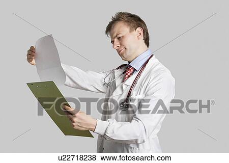 Male doctor in a lab coat reading medical records over gray background View Large Photo Image Stock Photo - Male doctor in a lab coat reading medical records over gray background. Fotosearch