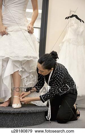Stock Photo - Mature female employee helping bride with footwear in bridal boutique. Fotosearch