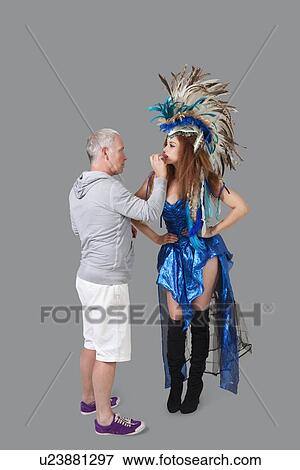 Stock Photo - Mature makeup artist grooming fashion model during photo shoot over gray background. Fotosearch