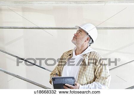 Stock Image - Mature male architect making a note in digital tablet while looking up at construction site. Fotosearch