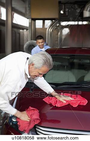 Stock Photo - mature owner and young employee wiping vehicle with cloth in car wash. Fotosearch