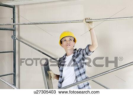 Mid adult female architect looking up while standing under scaffold at construction site View Large Photo Image Stock Image - Mid adult female architect looking up while standing under scaffold at construction site. Fotosearch