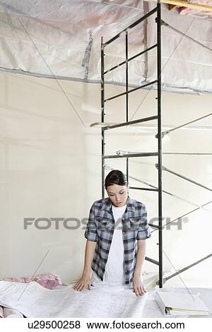 Stock Photo - Mid adult female contractor looking at blueprints. Fotosearch