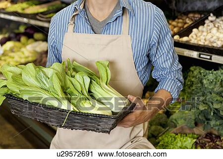 Stock Image - Midsection of man holding basket of bok choy in supermarket. Fotosearch