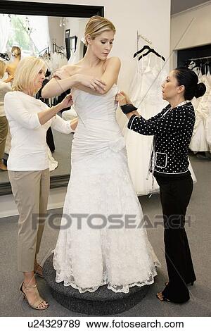 Stock Photo - Mother and store employee assisting young woman getting dressed in bridal store. Fotosearch