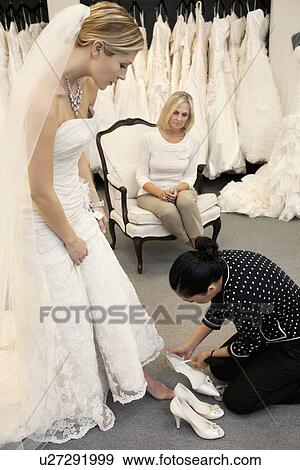 Stock Photo - Mother looking as female employee assisting young daughter in footwear. Fotosearch