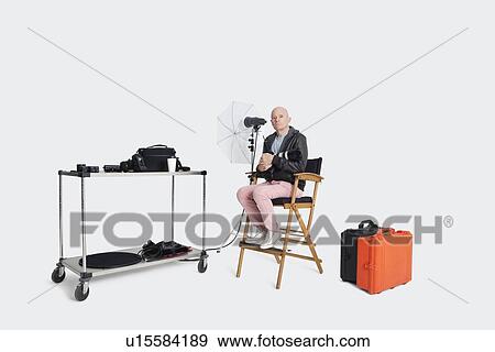 Stock Photo - Photographer sitting on director's chair with equipments in studio. Fotosearch