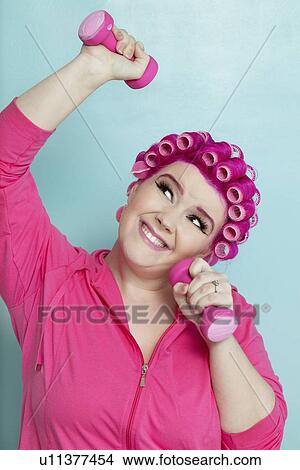 Playful young woman lifting weights over colored background View Large Photo Image Picture - Playful young woman lifting weights over colored background. Fotosearch