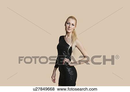 Stock Photo - Portrait of a beautiful blond woman wearing cocktail dress with hands on hips over colored background. Fotosearch