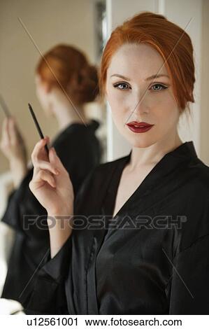 Stock Image - Portrait of a beautiful redheaded woman in robe holding a lip liner. Fotosearch
