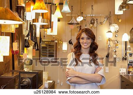 Picture - Portrait of a beautiful young woman with arms crossed standing in lights store. Fotosearch