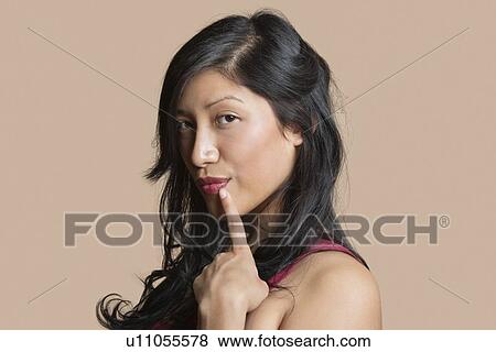 Stock Photo - Portrait of a beautiful young woman posing with finger on lip over colored background. Fotosearch