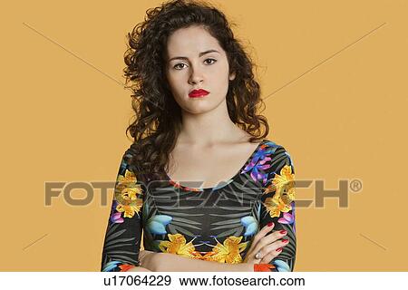 Stock Photo - Portrait of a confident young woman with arms crossed over colored background. Fotosearch