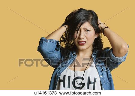 Stock Image - Portrait of a frustrated young woman with hands in hair over colored background. Fotosearch