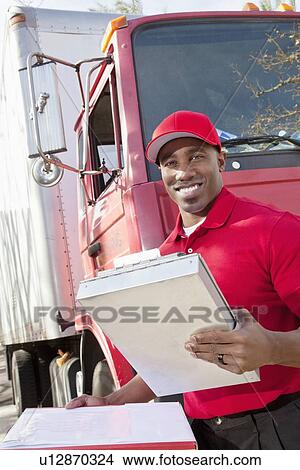 Picture - Portrait of a happy African American man holding clipboard with delivery truck in background. Fotosearch