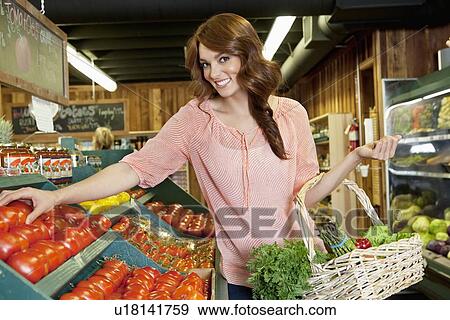 Stock Photo - Portrait of a happy brunette shopping for tomatoes in supermarket. Fotosearch