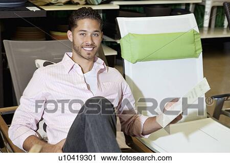 Stock Image - Portrait of a happy man sitting on chair in store. Fotosearch