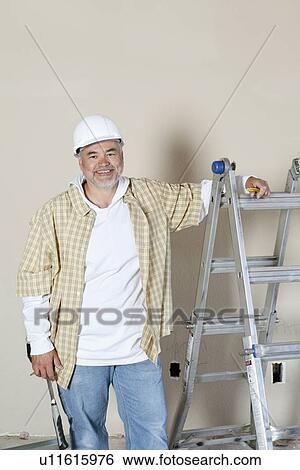 Stock Photograph - Portrait of a happy mature man standing near ladder over colored background. Fotosearch
