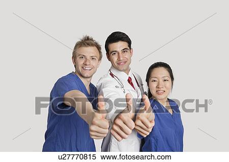 Stock Photography - Portrait of a happy medical team gesturing thumbs up over gray background. Fotosearch