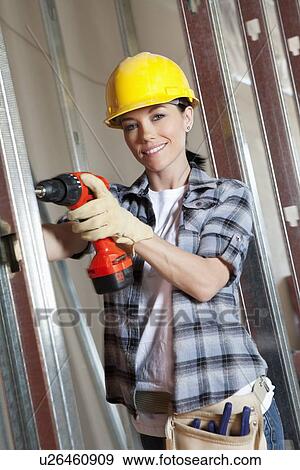 Stock Photo - Portrait of a happy mid adult woman worker drilling at construction site. Fotosearch