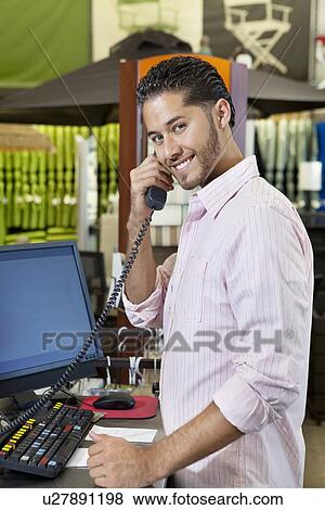 Stock Photo - Portrait of a happy salesperson listening to telephone receiver in store. Fotosearch