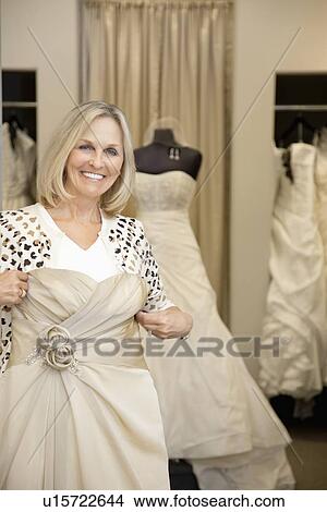 Portrait of a happy senior woman holding wedding gown in bridal store View Large Photo Image Picture - Portrait of a happy senior woman holding wedding gown in bridal store. Fotosearch