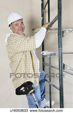 Stock Image - Portrait of a happy worker climbing scaffold. Fotosearch
