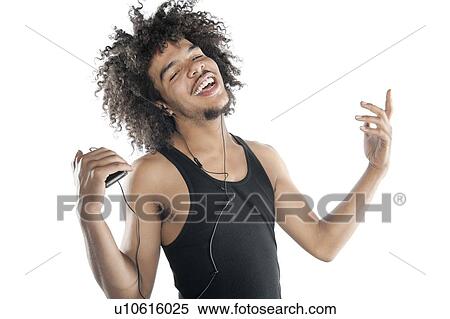Stock Photography - Portrait of a happy young man gesturing while listening to mp3 player over white background. Fotosearch