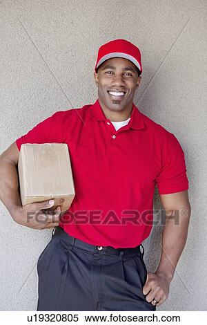 Portrait of a happy young man holding delivery box against wall View Large Photo Image Stock Photography - Portrait of a happy young man holding delivery box against wall. Fotosearch