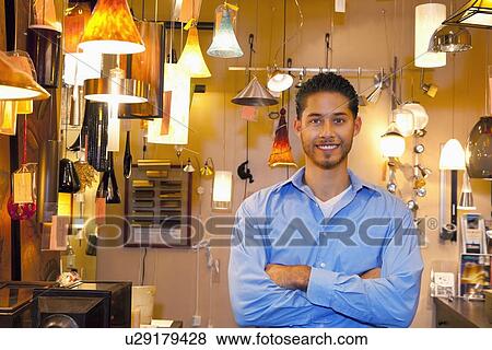 Stock Photo - Portrait of a happy young man with arms crossed in lights store. Fotosearch