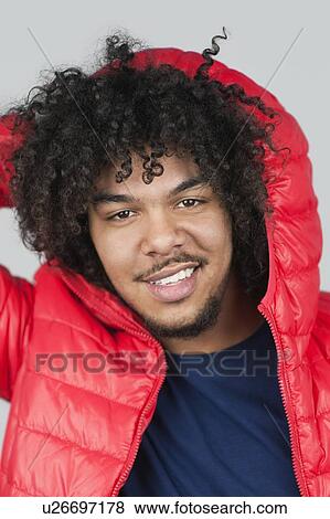 Stock Photo - Portrait of a happy young man with hood over colored background. Fotosearch