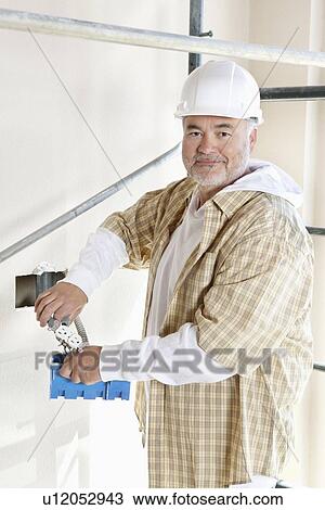 Stock Image - Portrait of a mature man holding construction equipment. Fotosearch